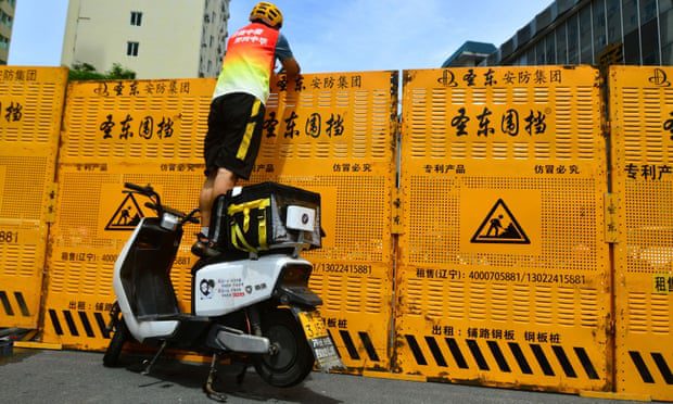 A courier standing on an electric bicycle to deliver goods across a roadblock in Sanya, Hainan Province