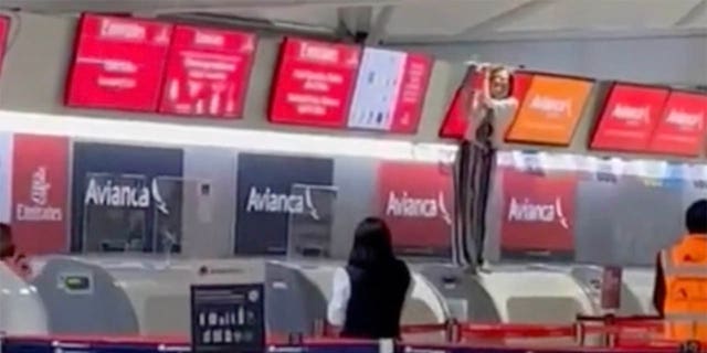 Other passengers at the airport can see the out-of-control person - standing at the check-in counter holding a screen above it - from afar.